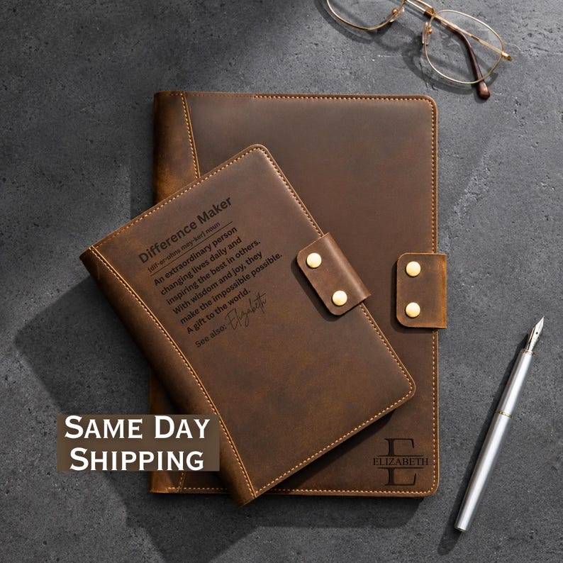 May include: Two brown leather journals with gold-tone snap closures. The smaller journal features the text: Difference Maker, An extraordinary person changing lives daily and inspiring the best in others. With wisdom and joy, they make the impossible possible. A gift to the world. See also: Elizabeth. The larger journal displays the letter E and the name Elizabeth. A silver pen and gold-rimmed glasses are included.