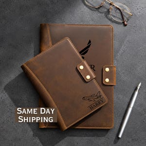 May include: Two brown leather journals with gold accents. One journal has a flap closure with two gold snaps. The smaller journal has an airplane graphic and the name "HARRY" engraved. A pen and glasses are also in the image.