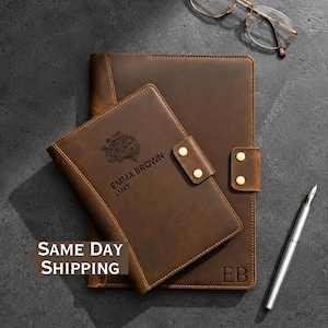 May include: A dark brown leather notebook and a smaller matching leather journal cover, both featuring gold-toned snap closures. The smaller journal is engraved with a floral brain illustration and the text EMMA BROWN LMFT, while the larger notebook has the initials EB.