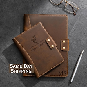 May include: Two brown leather notebooks with gold-tone snap closures. The smaller notebook features a director chair icon and the text "WRITTEN & DIRECTED BY: Mark Smith," while the larger notebook is embossed with the initials "MS" in the corner.