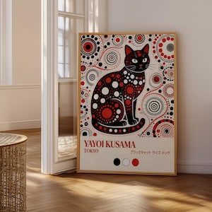 May include: A framed art print depicting a black cat with red and white polka dots and circles. The print includes the text "YAYOI KUSAMA TOKYO" and Japanese text. The artwork is displayed in a room with a wooden floor.