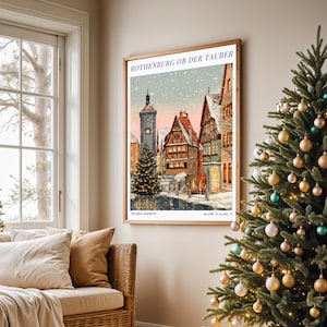 Puede incluir: Una lámina de arte mural enmarcada que representa una escena invernal nevada en Rothenburg ob der Tauber, Alemania. La ilustración muestra edificios tradicionales de entramado de madera, una torre de reloj y un árbol de Navidad iluminado.