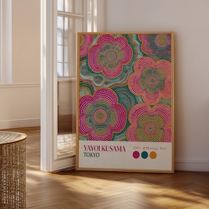 May include: A framed art print with a floral design in pink, teal, and yellow. The artwork includes the text "YAYOI KUSAMA TOKYO". The print is displayed in a room with wooden flooring. The artwork is in a wooden frame.