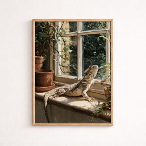 May include: A framed art print depicting a bearded dragon lizard resting on a wooden windowsill. The lizard is positioned near a window with green foliage visible outside. Two terracotta pots with plants are placed on the sill nearby.