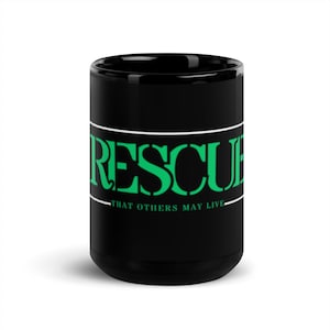 May include: A black coffee mug with the word "RESCUE" in green block letters, outlined in white. Below the word is the phrase "THAT OTHERS MAY LIVE" in white. The mug is glossy.
