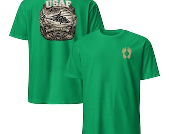 May include: Two green t-shirts. One features a detailed graphic on the back with the text "USAF" above a helicopter image and "COMBAT SEARCH & RESCUE" below. The other shirt has two tan footprints on the front.