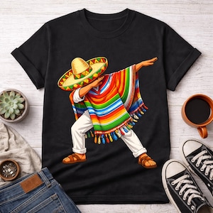 Puede incluir: Camiseta negra con una colorida ilustración de una persona haciendo dab, usando un sombrero y un poncho vibrante. El diseño incluye un sombrero amarillo, un poncho multicolor, pantalones blancos y sandalias marrones. Es una prenda de vestir casual.