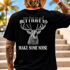 Peut inclure: Un t-shirt noir à manches courtes avec un motif blanc représentant un cerf rugissant aux grands bois. Le texte indique : some days are quiet BUT I HAVE TO MAKE SOME NOISE. Le motif est centré au dos du vêtement avec un aspect vieilli.