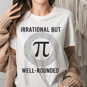 Peut inclure: T-shirt blanc avec le texte "IRRATIONAL BUT WELL-ROUNDED". Le t-shirt présente le symbole pi noir à l'intérieur d'un cercle pointillé. Le texte est en gras, en police sans-serif.