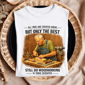 Könnte beinhalten: Weißes T-Shirt mit einer Grafik eines älteren Mannes, der Holz bearbeitet. Der Text auf dem Shirt lautet: „ALLE MÄNNER SIND GLEICH GESCHAFFEN, ABER NUR DIE BESTEN MACHEN IN IHREN SIEBZIGERN NOCH HOLZARBEITEN“.
