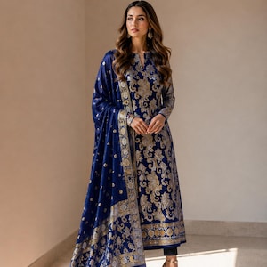 Könnte beinhalten: Eine tiefblaue, langärmelige Tunika mit einem komplizierten floralen Brokatmuster in Gold und Silber, kombiniert mit einem passenden blauen Dupatta-Schal mit breitem Metallic-Rand. Das Set wird mit einer schwarzen Hose und goldenen Absätzen getragen.