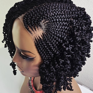 May include: A black braided wig with a curly texture, styled on a mannequin head. The wig features a lace front for a natural look. The mannequin is wearing a red and silver statement necklace.