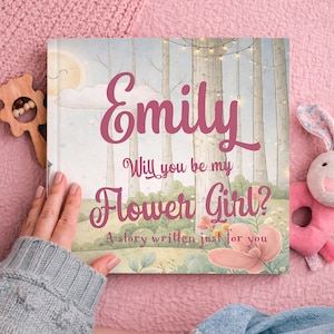 May include: A personalised children's book with the name "Emily" in large, cursive letters. The cover features a forest scene with the text "Will you be my Flower Girl?" and "A story written just for you."