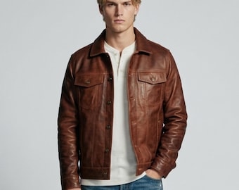 May include: A brown leather jacket with a pointed collar, long sleeves, and a button-front closure. The jacket features two chest pockets with buttoned flaps and vertical seam detailing on the front, worn over a white henley shirt and blue jeans.