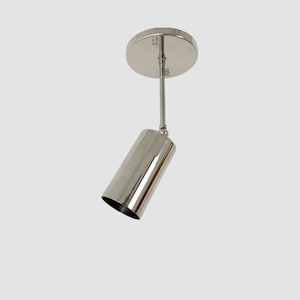 Könnte beinhalten: Ein Strahler mit poliertem Nickel-Finish, bestehend aus einem runden Deckenbaldachin, einer schlanken vertikalen Stange und einem zylindrischen Leuchtenkopf, der über ein Drehgelenk befestigt ist und eine verstellbare Ausrichtung ermöglicht.
