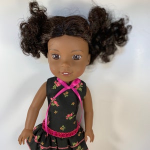 Può includere: Una bambola con la pelle scura e i capelli castani ricci raccolti in due codini. La bambola indossa un vestito nero con un motivo floreale rosa e un nastro rosa. L'abito ha una gonna a balze e una cintura rosa scintillante. La bambola indossa scarpe rosa.