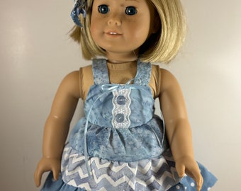 May include: A blue and white doll's dress with a layered skirt and a white lace trim. The dress has a blue button fastening at the top.