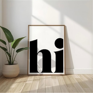 Könnte beinhalten: Ein gerahmter Kunstdruck mit dem Wort "hi" in fetten, schwarzen Buchstaben auf weißem Hintergrund. Der Druck befindet sich in einem Holzrahmen und lehnt an einer weißen Wand. Links steht eine Topfpflanze in einem geflochtenen Korb.