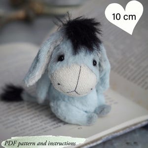 May include: A light blue plush donkey toy, approximately 4 inches tall, with a black mane and tail. The toy has a white muzzle and is sitting on an open book. Text on the image reads "PDF pattern and instructions."