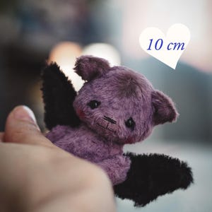 May include: A small purple and black plush bat toy with dark eyes and stitched facial features. A white heart graphic in the upper right corner displays the text 10 cm. A rectangular label at the bottom contains the text PDF PATTERN & INSTRUCTION.