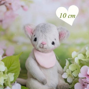May include: A handmade gray plush mouse with pink-lined ears and a pink bib, approximately 4 inches tall. The mouse is sitting on green grass surrounded by pink and white flowers. The image includes the text "PDF PATTERN".