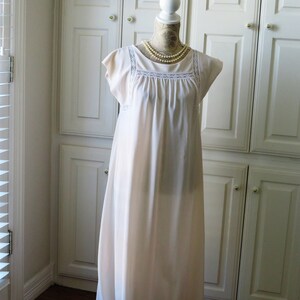 May include: A white, floor-length nightgown with a lace trim around the neckline and short sleeves. The nightgown is on a white mannequin with a pearl necklace.