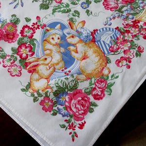 May include: White tablecloth with a colorful floral and bunny design. The design features pink, red, and blue flowers, along with illustrations of rabbits wearing hats. A basket of eggs is also depicted.