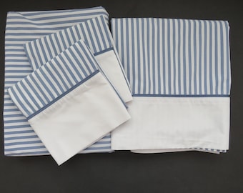 May include: A bedding set featuring a flat sheet, fitted sheet, and two pillowcases. The sheets have a blue and white striped pattern with a white border. The pillowcases have a white border with a blue trim. The set is made of a soft, comfortable material.