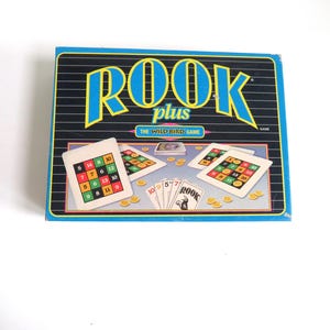 May include: A blue and white box for the Rook Plus card game. The box shows a game board with cards and chips. The text on the box reads "Rook Plus The Wild Bird Game".
