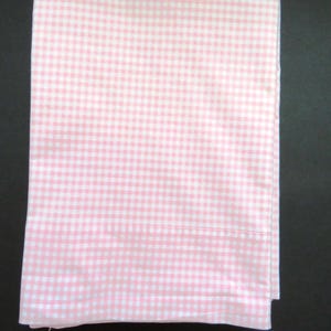 Puede incluir: Una sábana doblada con un estampado de cuadros vichy rosa y blanco. La tela es suave y tiene un dobladillo cosido. El diseño es un diseño de cuadros pequeños clásico. La sábana es probablemente para una cama.