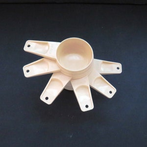 Puede incluir: Un juego de tazas y cucharas medidoras beige dispuestas en forma de estrella. Las tazas y cucharas son de plástico y de varios tamaños. Diseñado para medir ingredientes en la cocina.