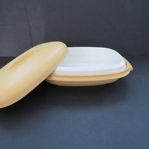 Könnte beinhalten: Ein gelber Plastik-Dampfgarer mit Deckel. Der Dampfgarer hat eine weiße Innenschale mit Löchern zum Dämpfen von Speisen.