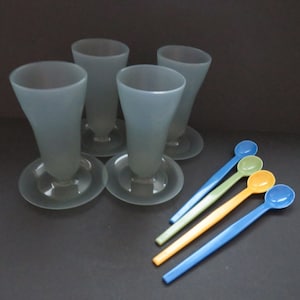 May include: Four frosted glass cups with a flared base and four plastic spoons in blue, green, and yellow.