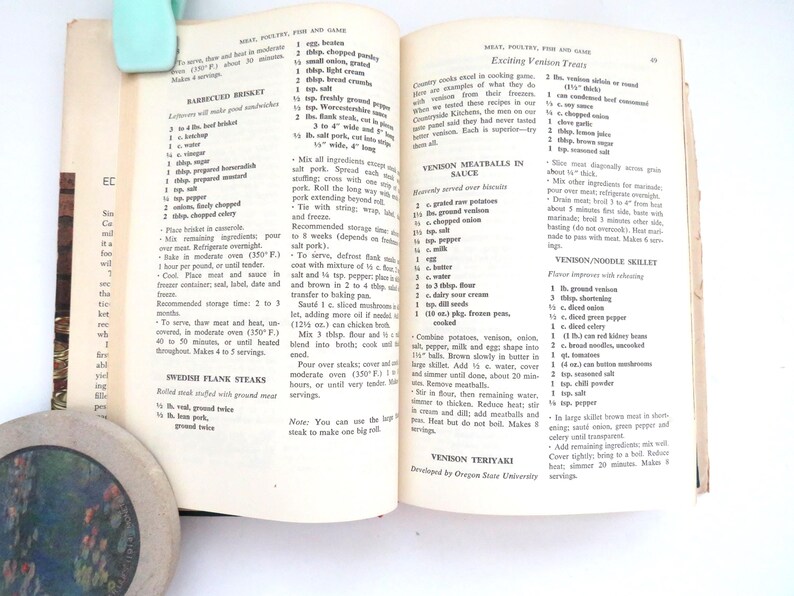 May include: An open cookbook page featuring recipes for Barbecued Brisket, Swedish Flank Steaks, Venison Meatballs in Sauce, and Venison Teriyaki. The text is printed in black ink on off-white paper with visible page numbers and column headers.