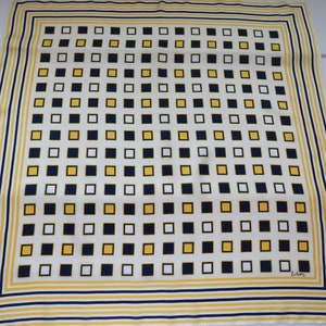 May include: A white silk scarf with a yellow and navy blue geometric pattern. The scarf has a thin yellow border and a thicker navy blue border. The pattern is made up of small squares. The scarf is signed "Echarpe" in the bottom right corner.