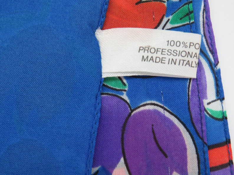 Może przedstawiać: Biała metka z tekstem "100% PO PROFESSIONAL MADE IN ITALY" na niebieskim i białym materiale z kolorowym wzorem owoc&oacute;w.