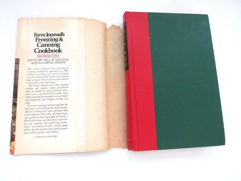 May include: A hardcover book titled Farm Journal's Freezing & Canning Cookbook with a dark green cover and a red spine. The book is displayed with its detached, cream-colored paper dust jacket laid flat to the left, showing printed text.