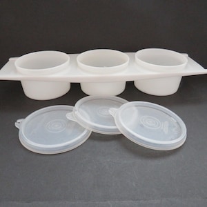 Puede incluir: Contenedor de plástico blanco de tres secciones con tapas. El contenedor tiene tres compartimentos individuales para guardar objetos pequeños. Las tapas son de plástico transparente.