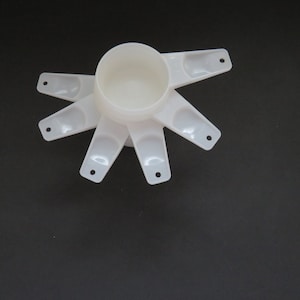Puede incluir: Juego de tazas medidoras de plástico blanco de diferentes tamaños, dispuestas en forma de estrella.