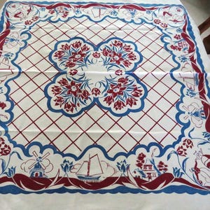Puede incluir: Un mantel blanco con un diseño holandés en rojo y azul. El mantel presenta molinos de viento, tulipanes y casas.