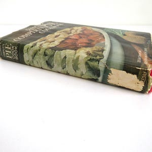 Puede incluir: Libro de cocina vintage de tapa dura titulado "The Complete Pie Cookbook" con una foto de un pastel en la portada. La portada es verde, marr&oacute;n y blanca con una lomo rojo.