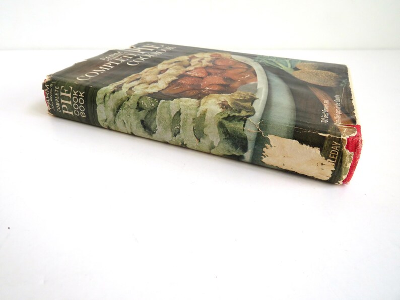 Puede incluir: Libro de cocina vintage de tapa dura titulado "The Complete Pie Cookbook" con una foto de un pastel en la portada. La portada es verde, marr&oacute;n y blanca con una lomo rojo.