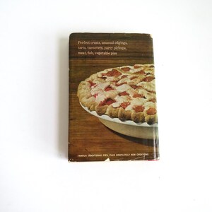 Puede incluir: Una portada de libro de cocina vintage con un primer plano de una tarta de cerezas con una corteza escamosa. El texto en la portada dice "Perfect crusts, unusual edgings, tarts, turnovers, party pickups, meat, fish, vegetable pies. Famous traditional pies plus completely new creations."