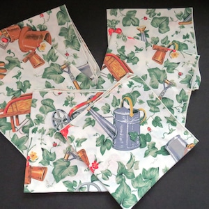 Puede incluir: Conjunto de cuatro toallas de té de algodón blanco con un patrón de hiedra verde y herramientas de jardinería. Las herramientas incluyen una carretilla, una regadera, una pala y un rastrillo. Las toallas tienen un borde blanco.