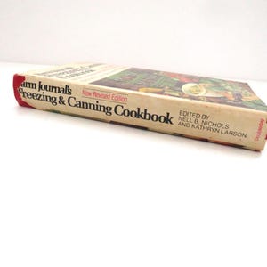 May include: A vintage Farm Journal's Freezing & Canning Cookbook, New Revised Edition, edited by Nell B. Nichols and Kathryn Larson. The book has a cream-colored spine and cover with black text and a red accent, published by Doubleday.