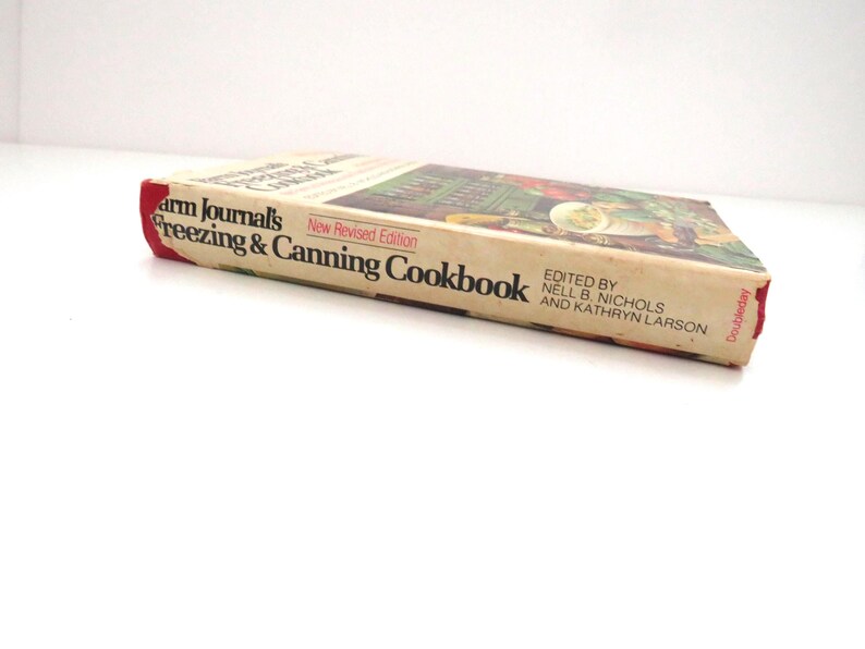 May include: A vintage Farm Journal's Freezing & Canning Cookbook, New Revised Edition, edited by Nell B. Nichols and Kathryn Larson. The book has a cream-colored spine and cover with black text and a red accent, published by Doubleday.