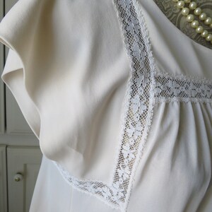 May include: A white sleeveless top with a lace trim around the neckline. The lace is a delicate floral pattern.