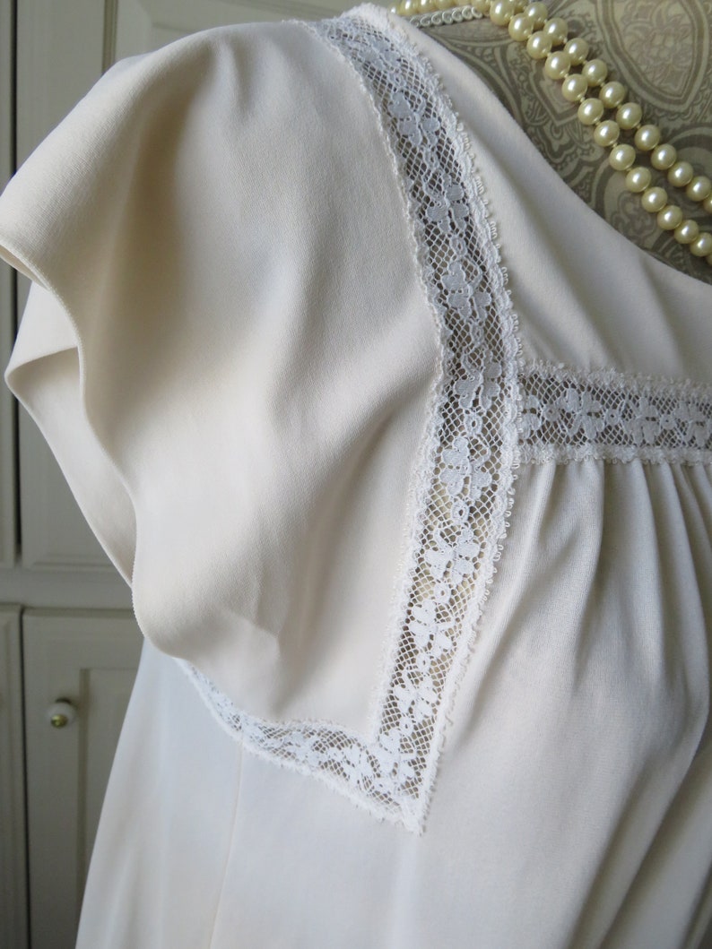 May include: A white sleeveless top with a lace trim around the neckline. The lace is a delicate floral pattern.