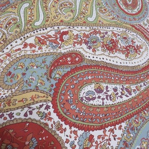 May include: Close-up of a fabric with a paisley pattern. The design features large, teardrop-shaped motifs in shades of red, orange, blue, yellow, and green, with intricate floral and scroll details. The background is white.
