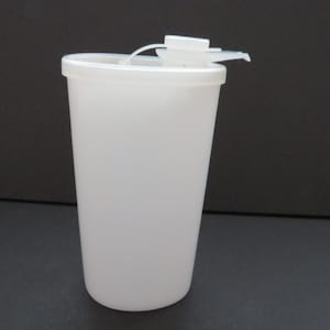 May include: A white plastic tumbler with a lid and a flip-top spout. The tumbler is cylindrical and has a smooth surface. The lid is attached to the tumbler with a small white plastic hinge. The spout is open.